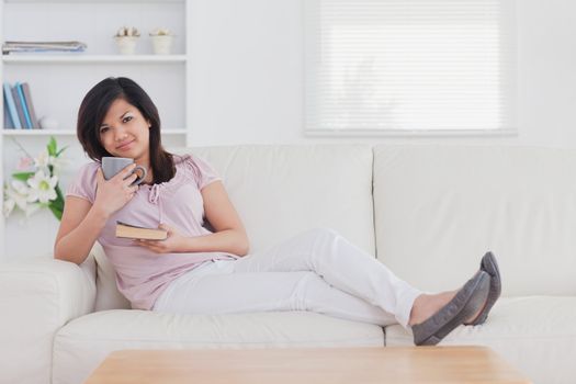 Woman sitting on a couch while holding a mug and a book in a living room