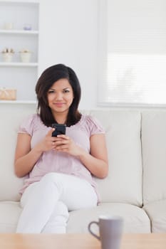 Woman sitting on a sofa while she is holding a phone in a living room
