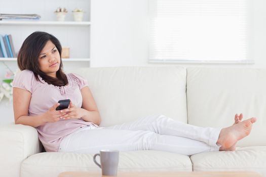 Barefoot woman lying on a couch while holding a telephone in a living room