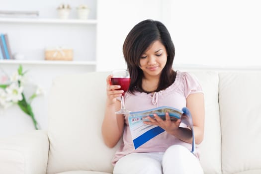 Woman holding a glass of red wine while reading a magazine in a living room