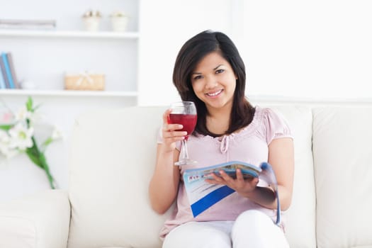 Woman holding a magazine while holding a glass of red wine in a living room