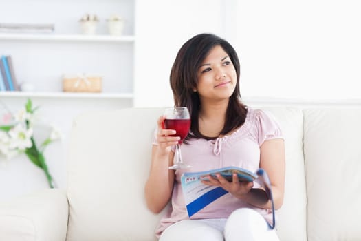 Woman holding a magazine and a glass of red wine in a living room