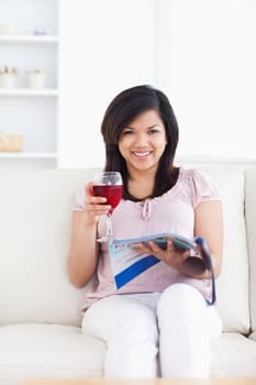 Woman looking ahead as she reads a magazine and holds a glass of red wine in a living room