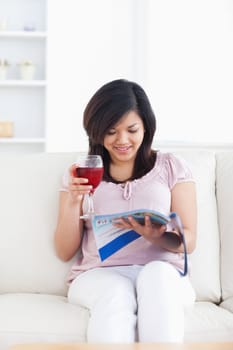 Woman resting on a sofa while reading a magazine and holding a red glass of wine in a living room