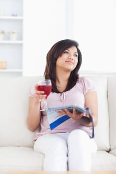 Woman sitting on a couch while holding a glass of red wine and a magazine in a living room