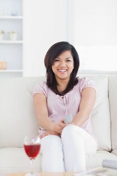Smiling woman sitting on a couch while holding a television remote