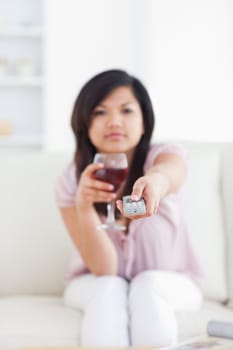 Blurred woman holding a glass of red wine and a television remote in a living room