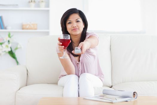 Woman holds a glass of wine and a television remote in a living room