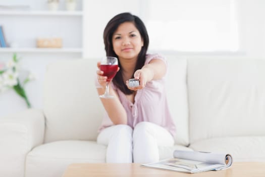 Woman holding a television remote and a glass of red wine in a living room