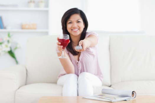 Woman sitting in a white couch while holding a glass of red wine and a television remote in a living room