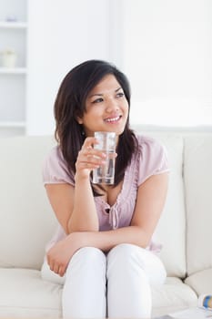 Woman sitting on a sofa and holding a glass of water in a living room