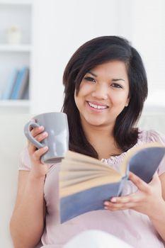 Woman smiling while holding a mug and a book in a living room
