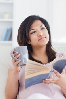 Woman sitting on a couch while holding a book and a mug in a living room