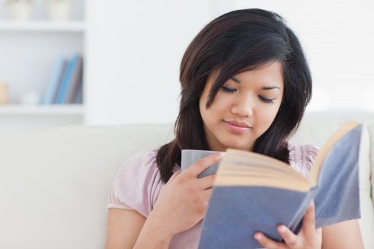 Woman reading a book while holding a cup in a living room