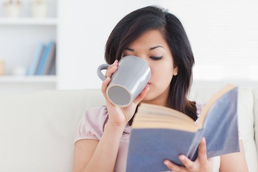 Woman drinking from a mug while holding a book in a living room