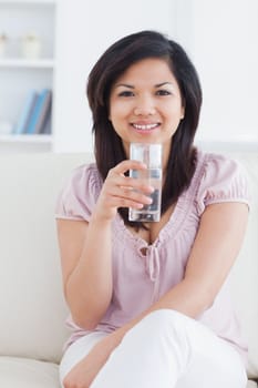 Woman smiling while sitting on a couch and holding a glass of water in a living room