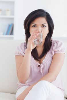 Woman sitting on a couch while drinking a glass of water in a living room
