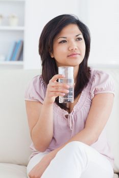Woman sitting on a couch while crossing her legs and holding a glass of water in a living room