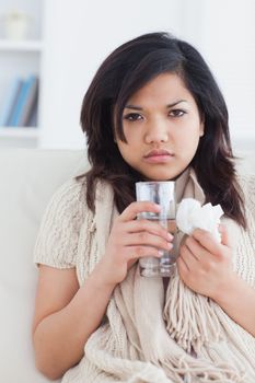 Sick woman holding a tissue and a glass of water in a living room