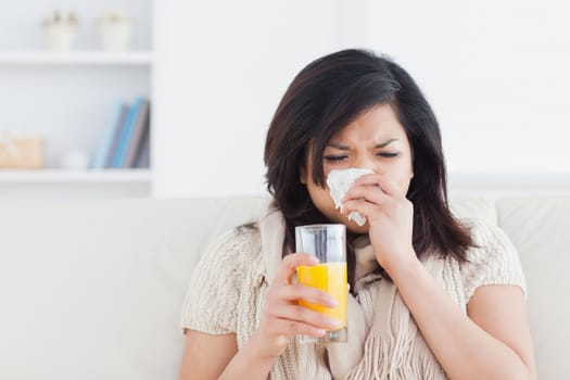 Sneezing woman drinking a glass of orange juice in a living room