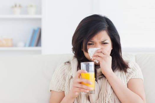 Woman holding a glass of orange juice while sneezing in a living room