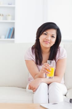 Woman sitting on a sofa while holding a glass of orange juice in a living room