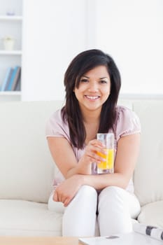 Smiling woman sitting and holding a glass of orange juice in a living room