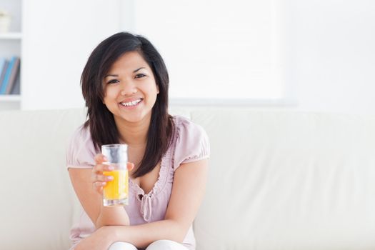 Woman smiling and sitting in a couch while holding a glass of orange juice in a living room