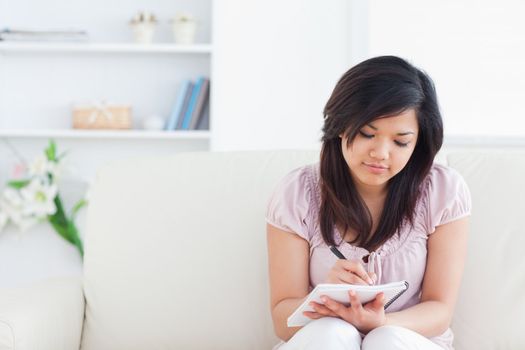 Woman sitting on a sofa while writing on a notebook in a living room