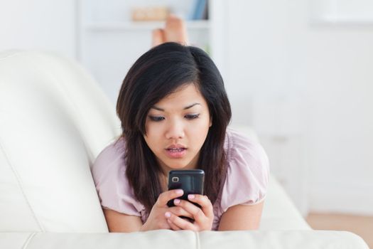 Surprised woman looking at a phone on a sofa in a living room