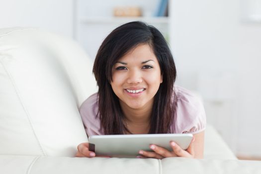 Woman smiling while resting on a couch and playing with a tablet in a living room