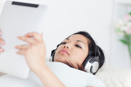 Woman lies on a coach and holds a tactile tablet with headphones on a living room