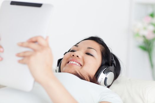 Smiling woman lying on a coach with headphones on and holding a tactile tablet in a living room