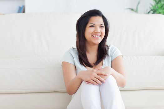 Woman smiles as she sits in front of a couch on the floor in a living room