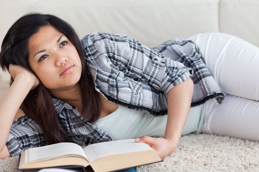 Thinking woman lying on the floor while holding a book in a living room