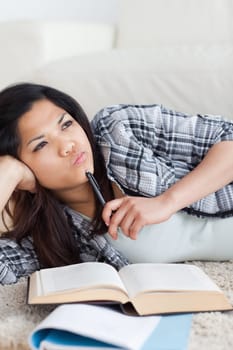 Close-up of a woman thinking while holding a pen and a book in a living room