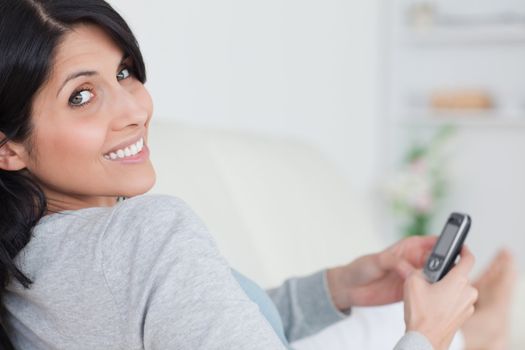 Smiling woman holding a phone while lying on a couch in a living room