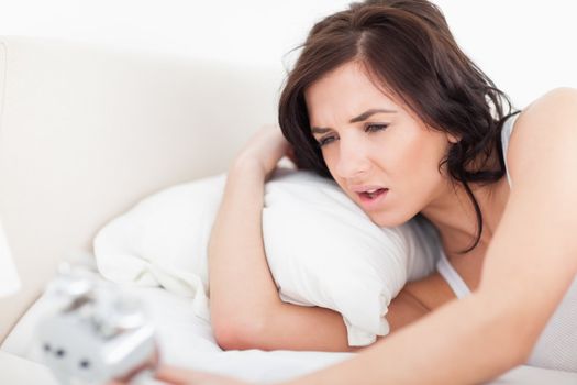 Brunette woman waking up while looking at her alarm clock in her bedroom
