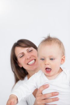 Smiling mother holding her surprised baby against a grey background