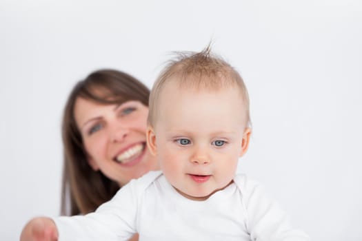 Smiling brunette woman holding her cute baby against a grey background