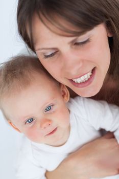 Cheerful mother holding her cute baby against a grey background