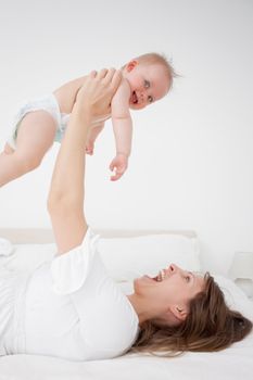 Happy woman holding her baby while lying in a bedroom