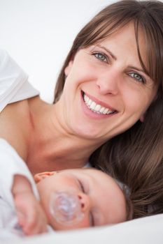 Smiling brunette woman lying while her baby is sleeping in a bedroom