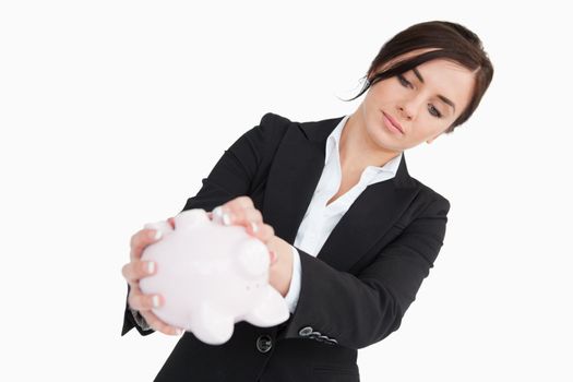 Young woman in suit emptying a piggy bank against white background