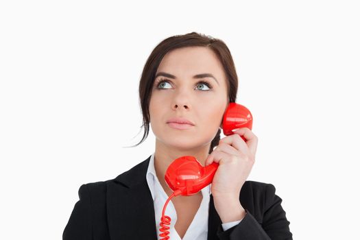 Woman in suit using a red dial telephone against white background