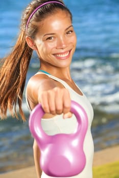 Kettlebell training woman doing cross strength training lifting kettlebell weights outside. Smiling happy Asian fitness model doing one-arm shoulder extensions.