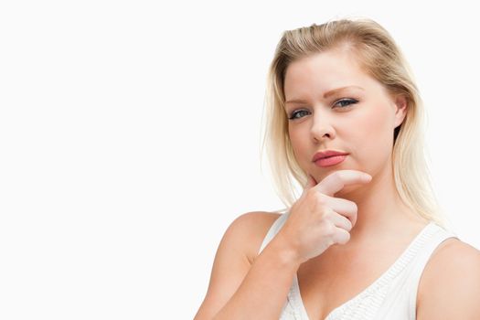 Serious blonde woman placing her hand on her chin against a white background