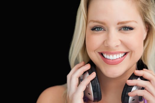 Smiling woman standing while holding her headphones against a black background