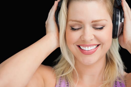 Smiling blonde woman wearing her headphones against a black background