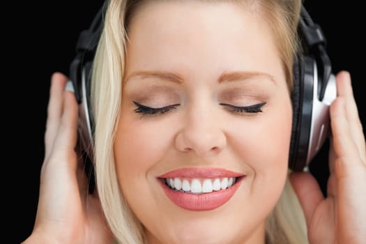 Cheerful woman closing her eyes while listening to music against a black background